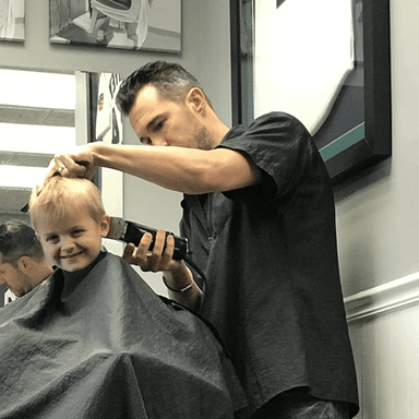 Barber cutting hair of young boy in salon