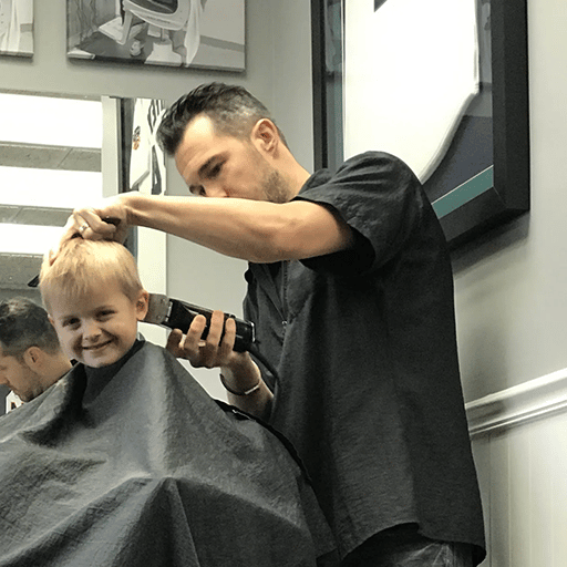 Barber cutting hair of young boy in salon